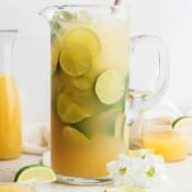 A pitcher of margaritas with limes and ice.
