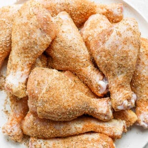 Several raw chicken legs covered in the smoked chicken dry rub on a white plate.