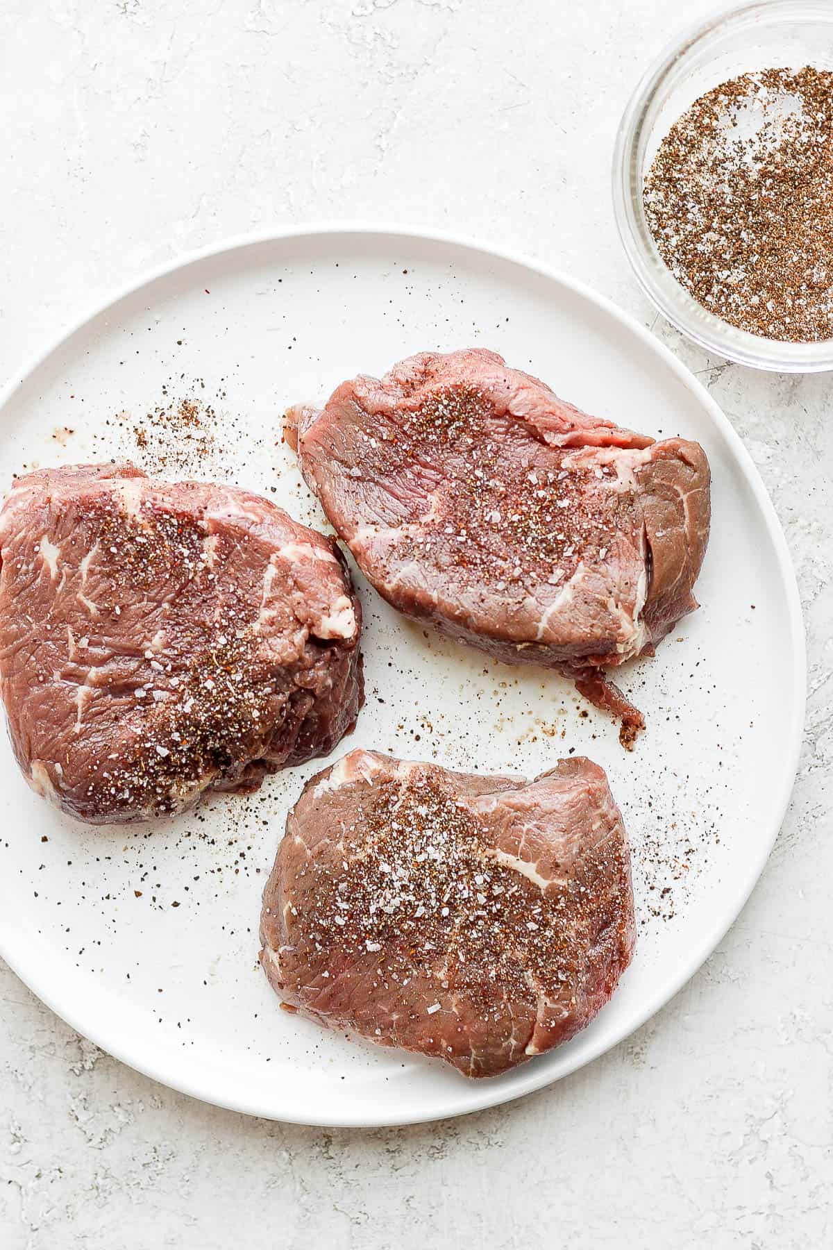 Three steaks on a plate with dry rub on top of the them. 