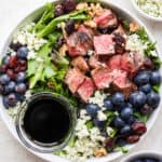 A bowl filled with a grilled steak salad with blueberries and blue cheese.
