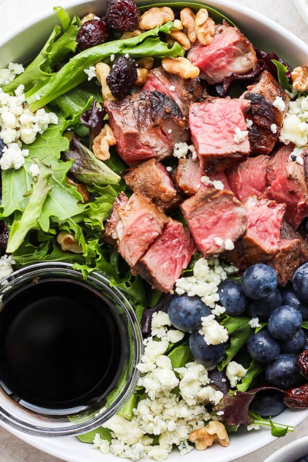 A bowl filled with a grilled steak salad with blueberries and blue cheese.