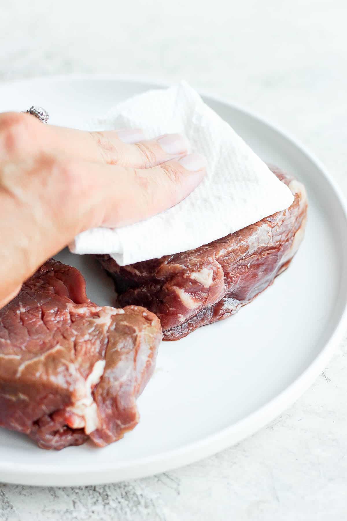 Someone patting dry steaks with a clean paper towel.