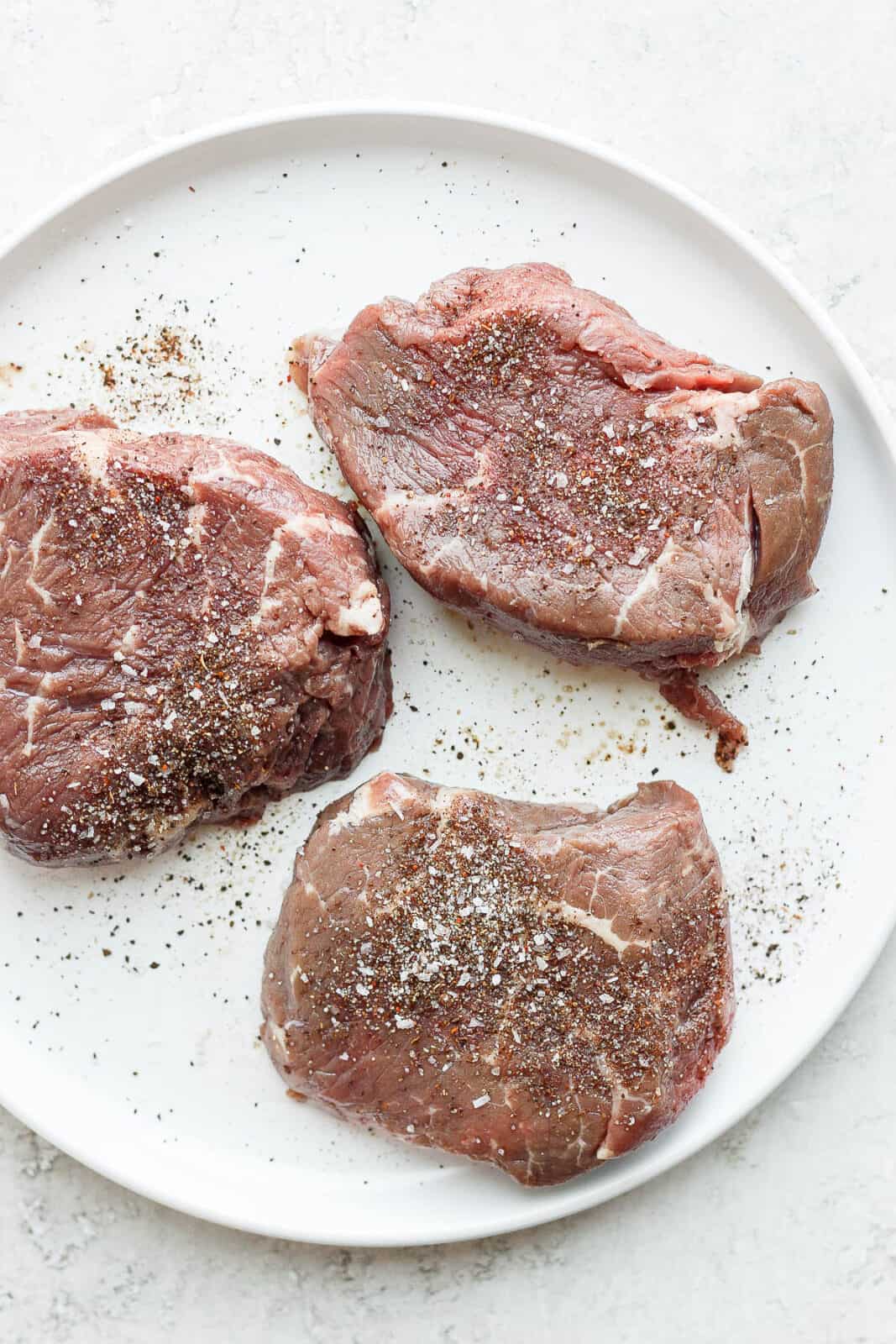 Three steaks on a plate with dry rub on them. 