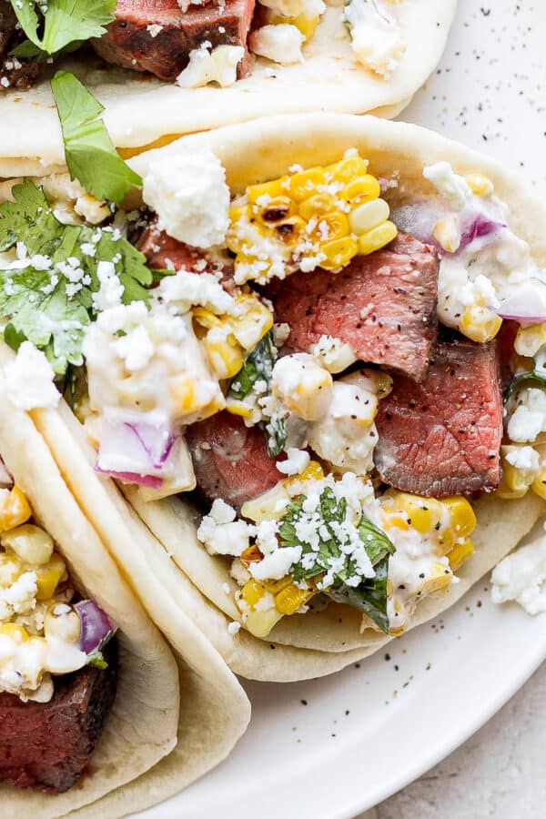 Grilled steak on street taco tortillas with Mexican street corn and other taco toppings.