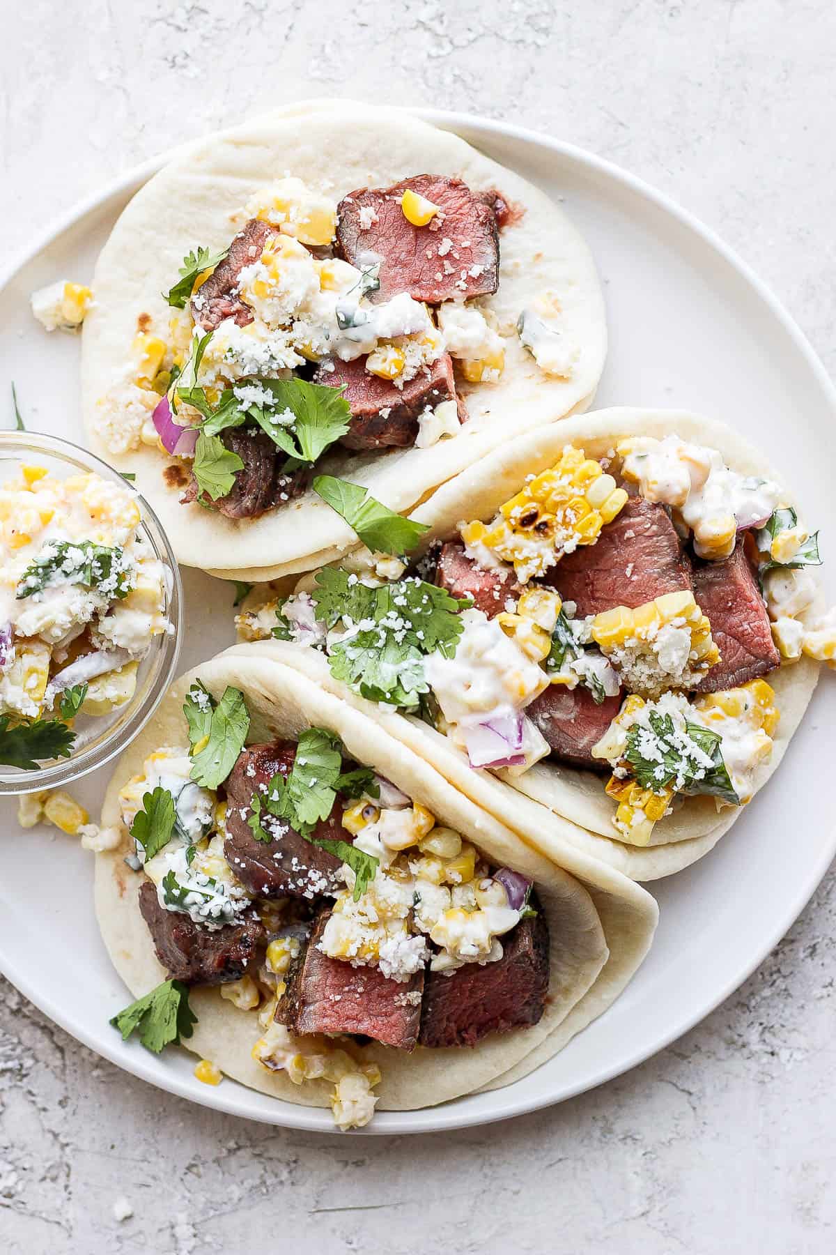 Assembled steak tacos on a white plate.