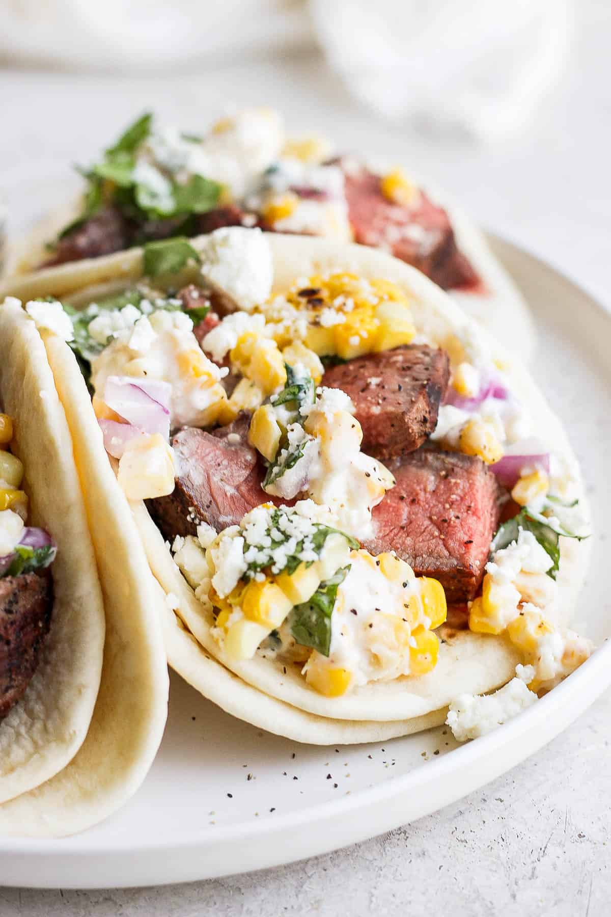 A straight-on shot of a steak taco with Mexican street corn salad and feta cheese.