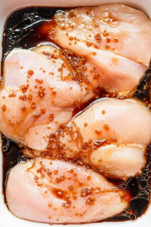 Raw chicken breasts sitting in a chicken marinade.