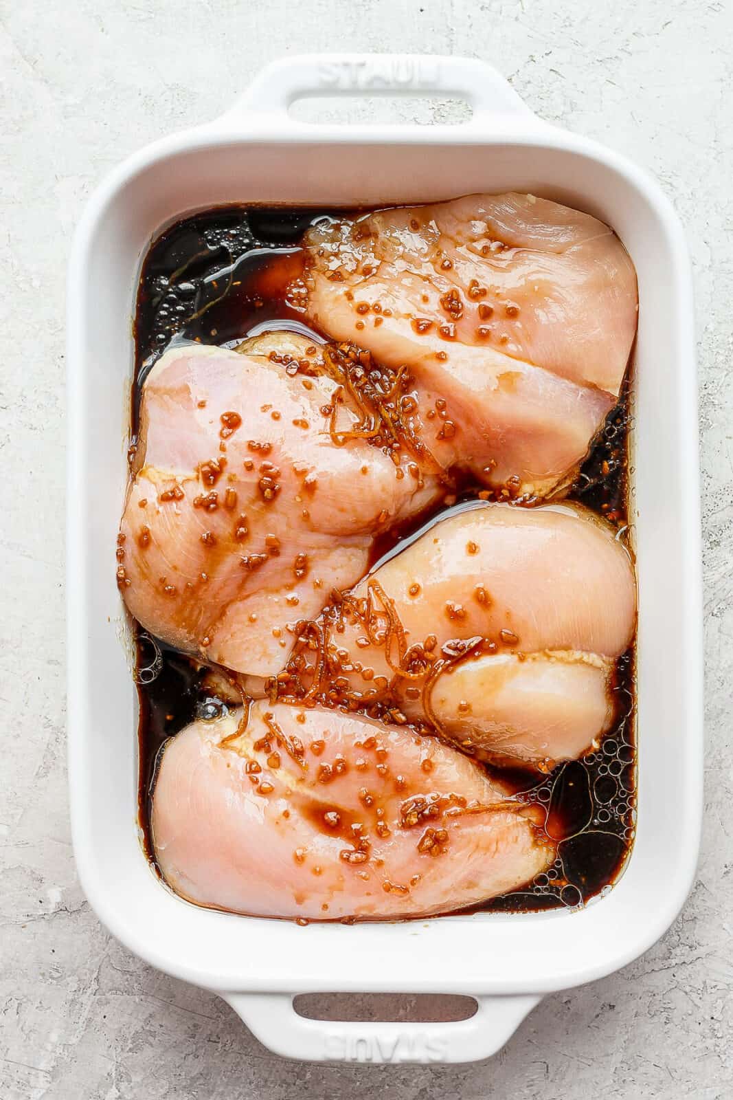 Four raw chicken breasts in a marinade. 