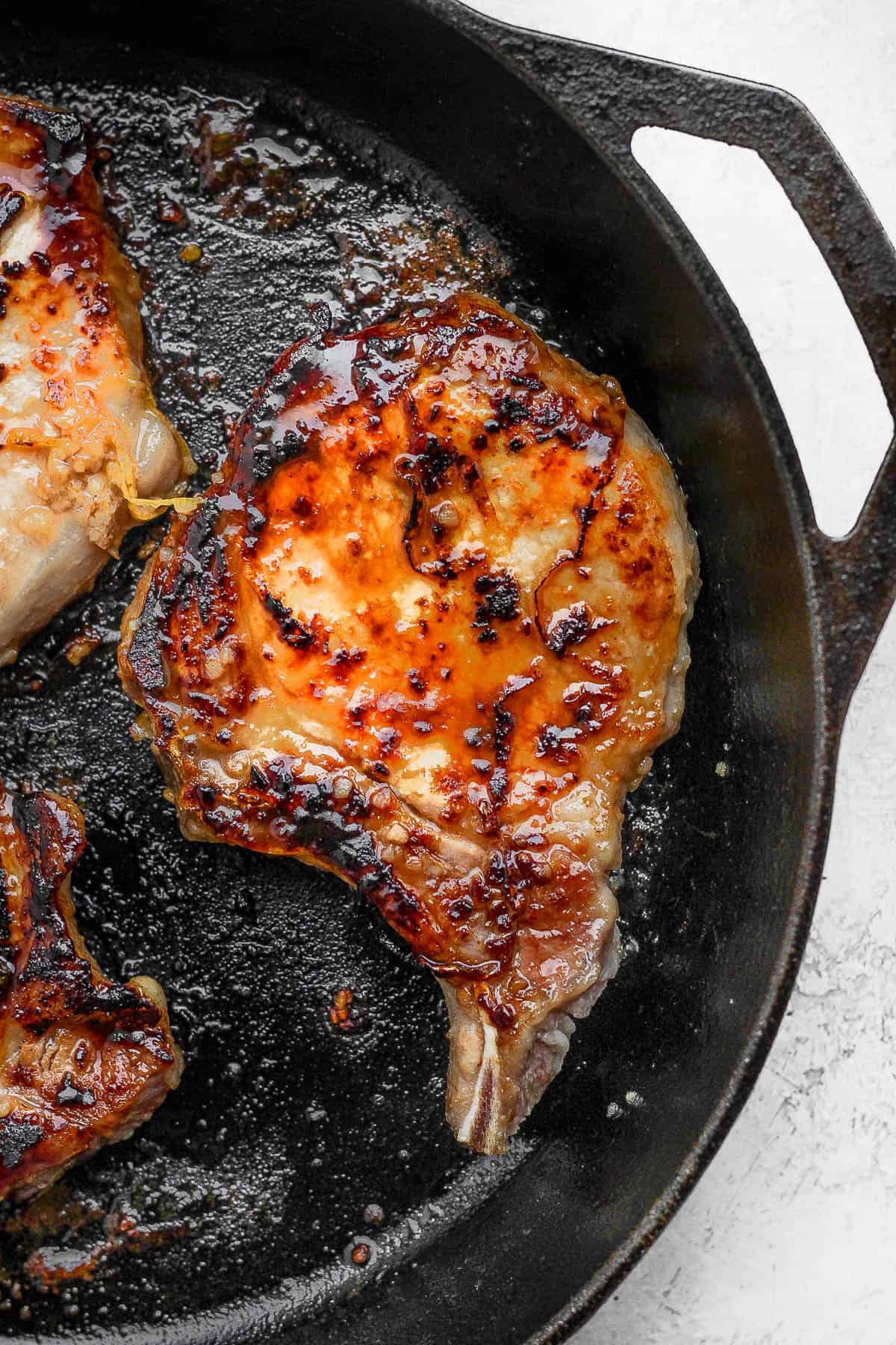 Pork chops cooking in a cast iron skillet.