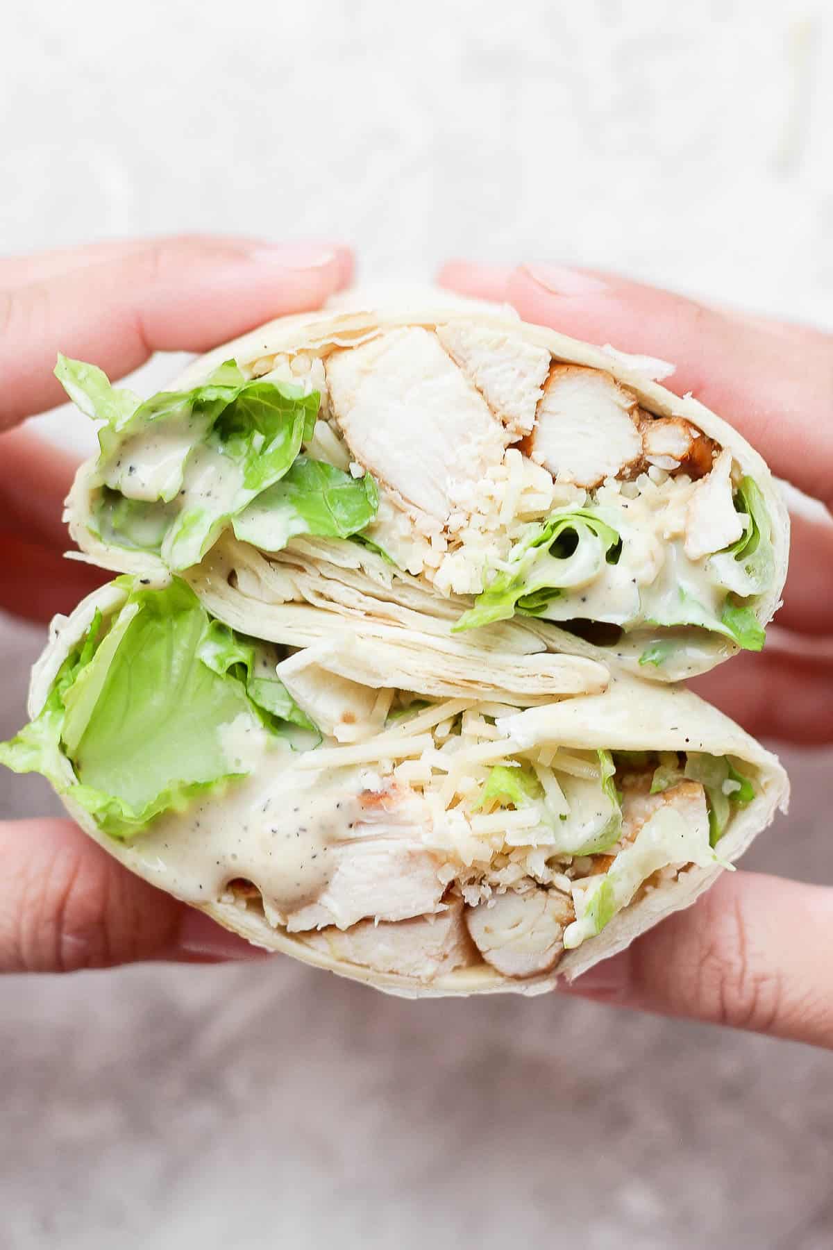 2 halves of a chicken caesar wrap being held open.