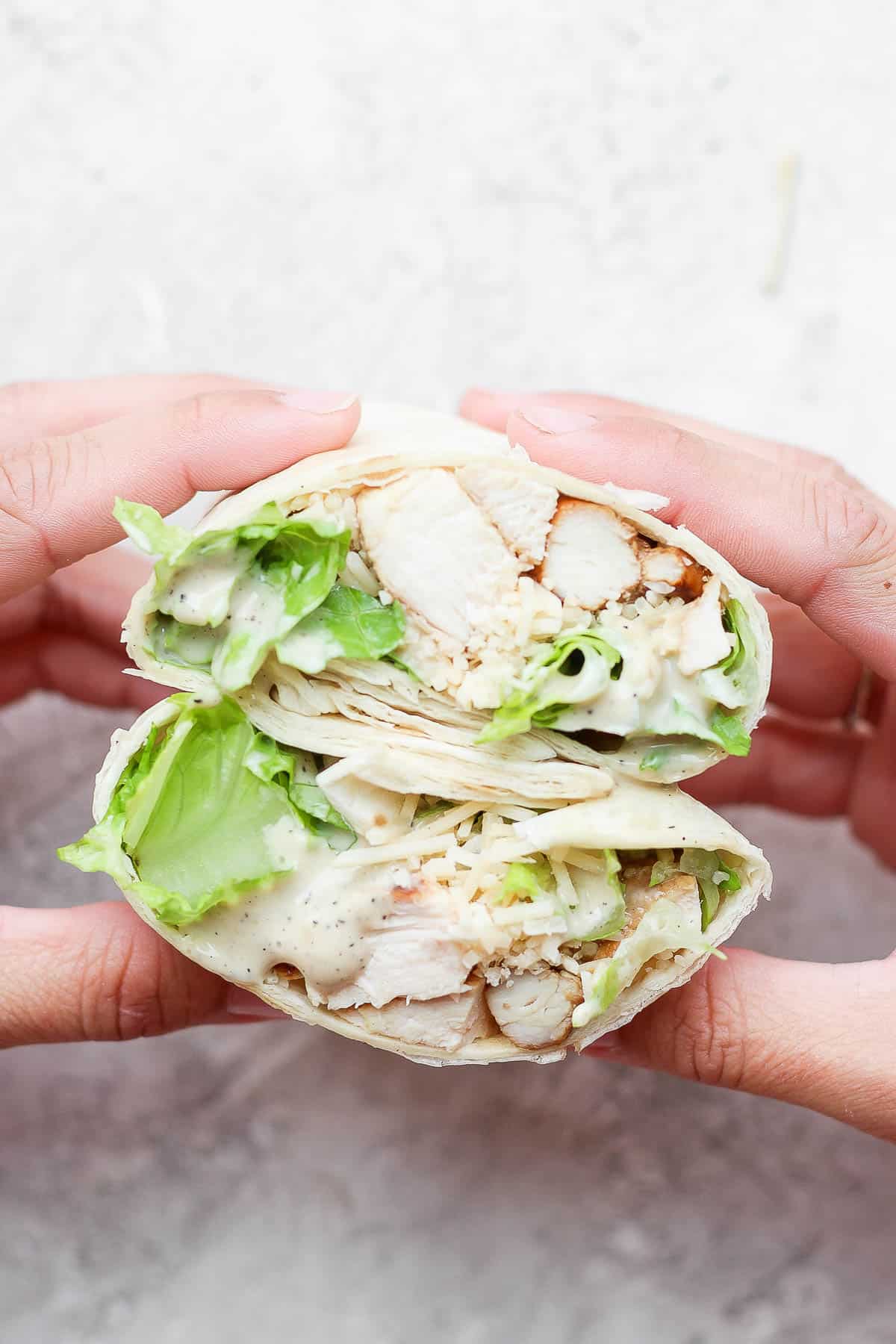 Hands holding a chicken caesar wrap that was cut open in the middle.