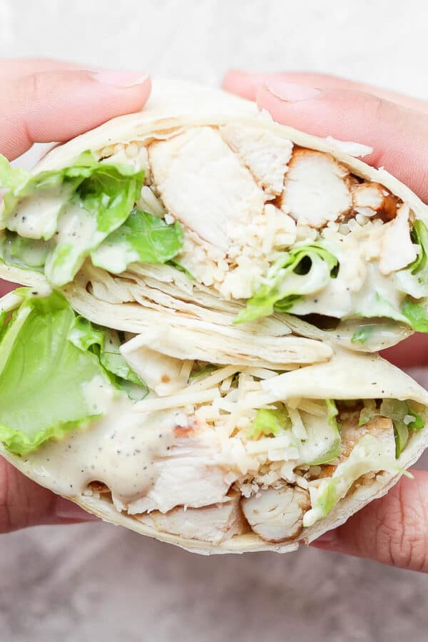 A chicken caesar wrap cut in half and being held by two hands.