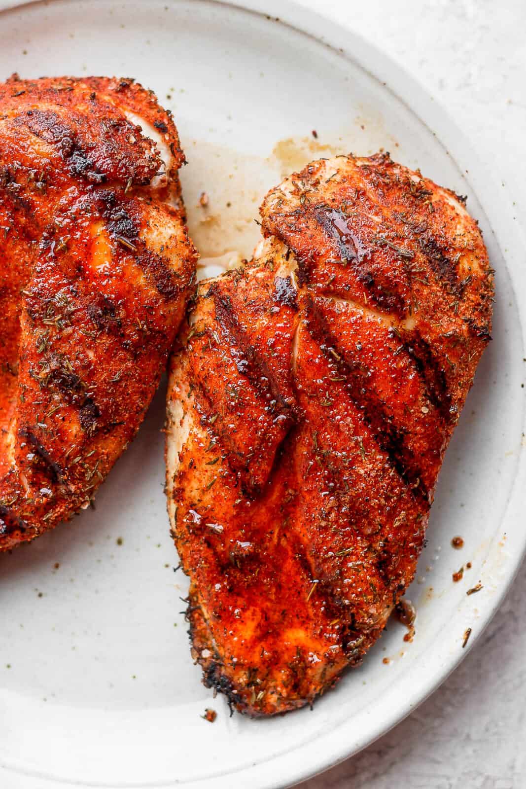 Seasoned chicken breasts that were grilled on a plate.