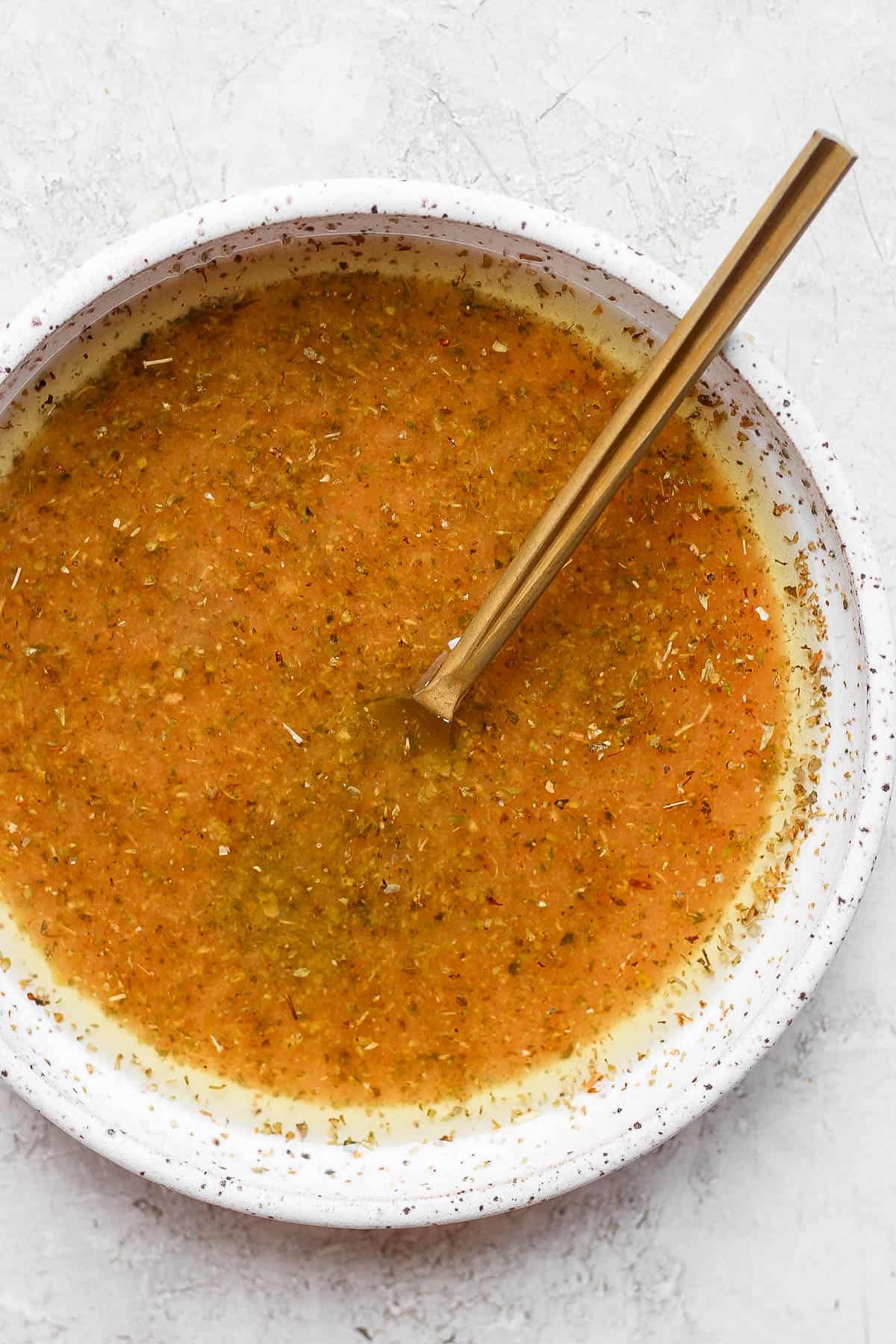 A bowl of greek vinaigrette with a spoon.