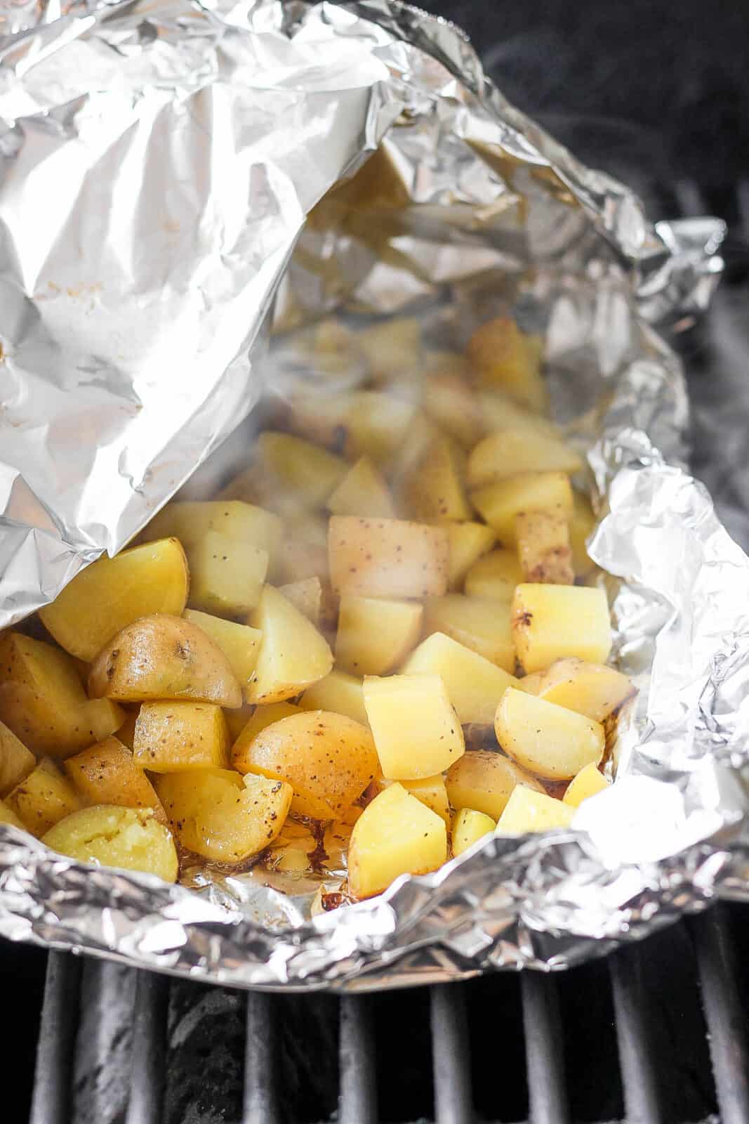 Grilled potatoes in a foil boat on the grill with one corner slightly open to see the steam.