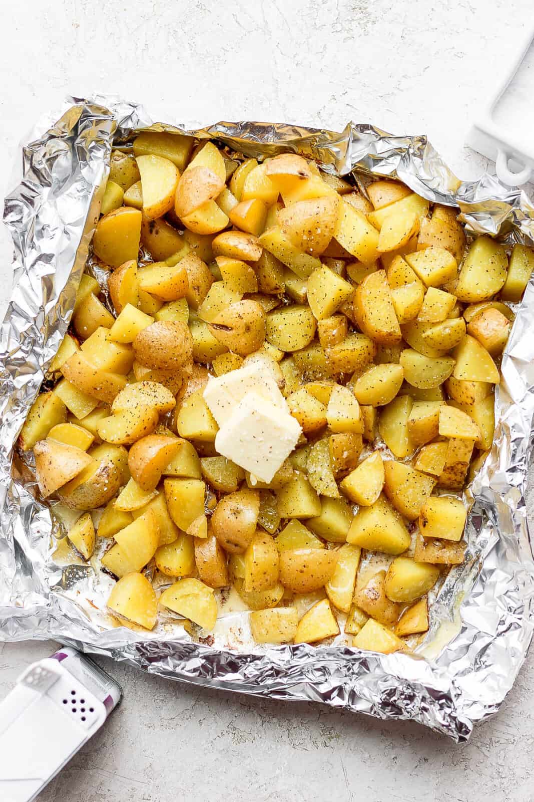 Grilled potatoes in foil boat with salt, pepper, and butter.