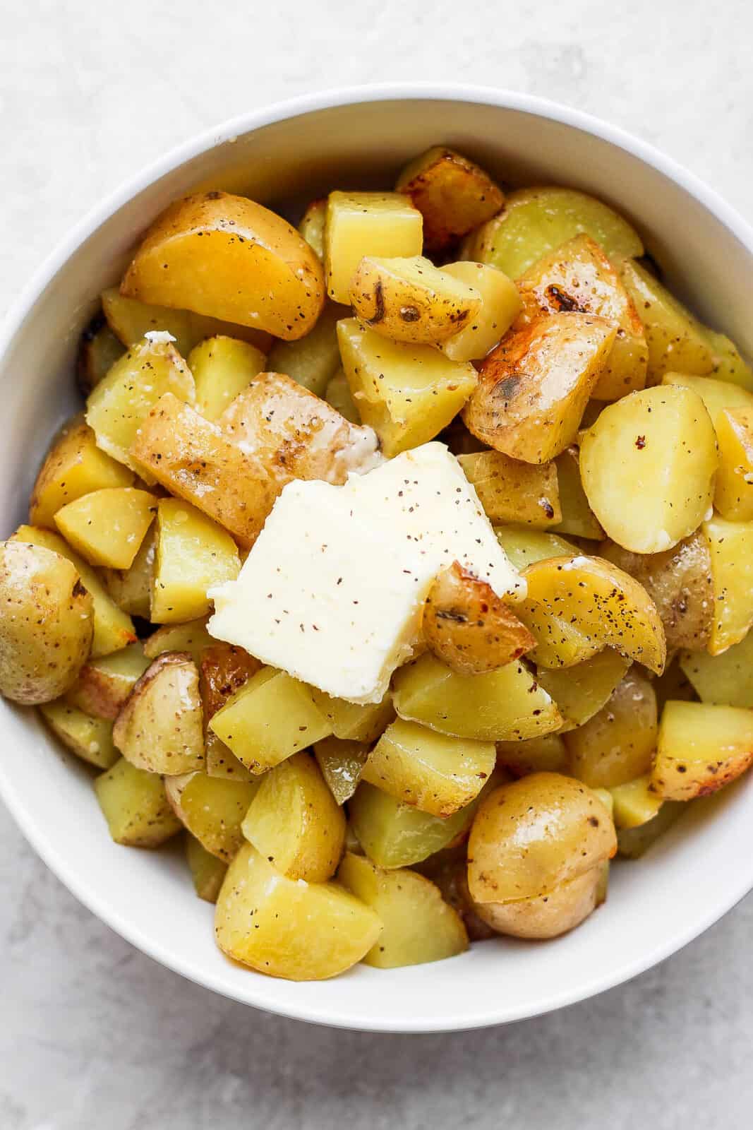 Grilled potatoes in a bowl with extra butter, salt, and pepper.