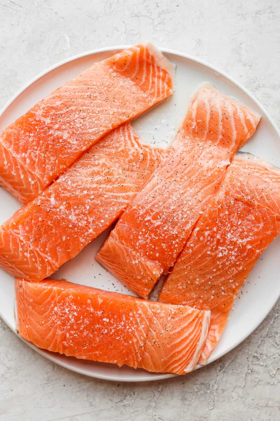 A large plate with salmon on it seasoned with salt and pepper. 