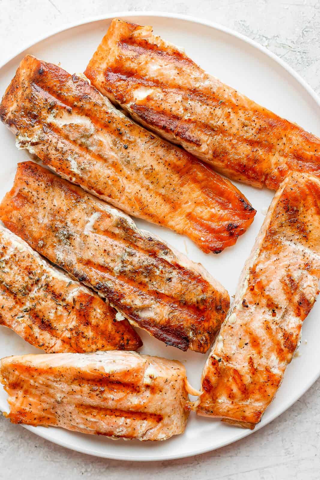 A large plate filled with grilled salmon fillets. 