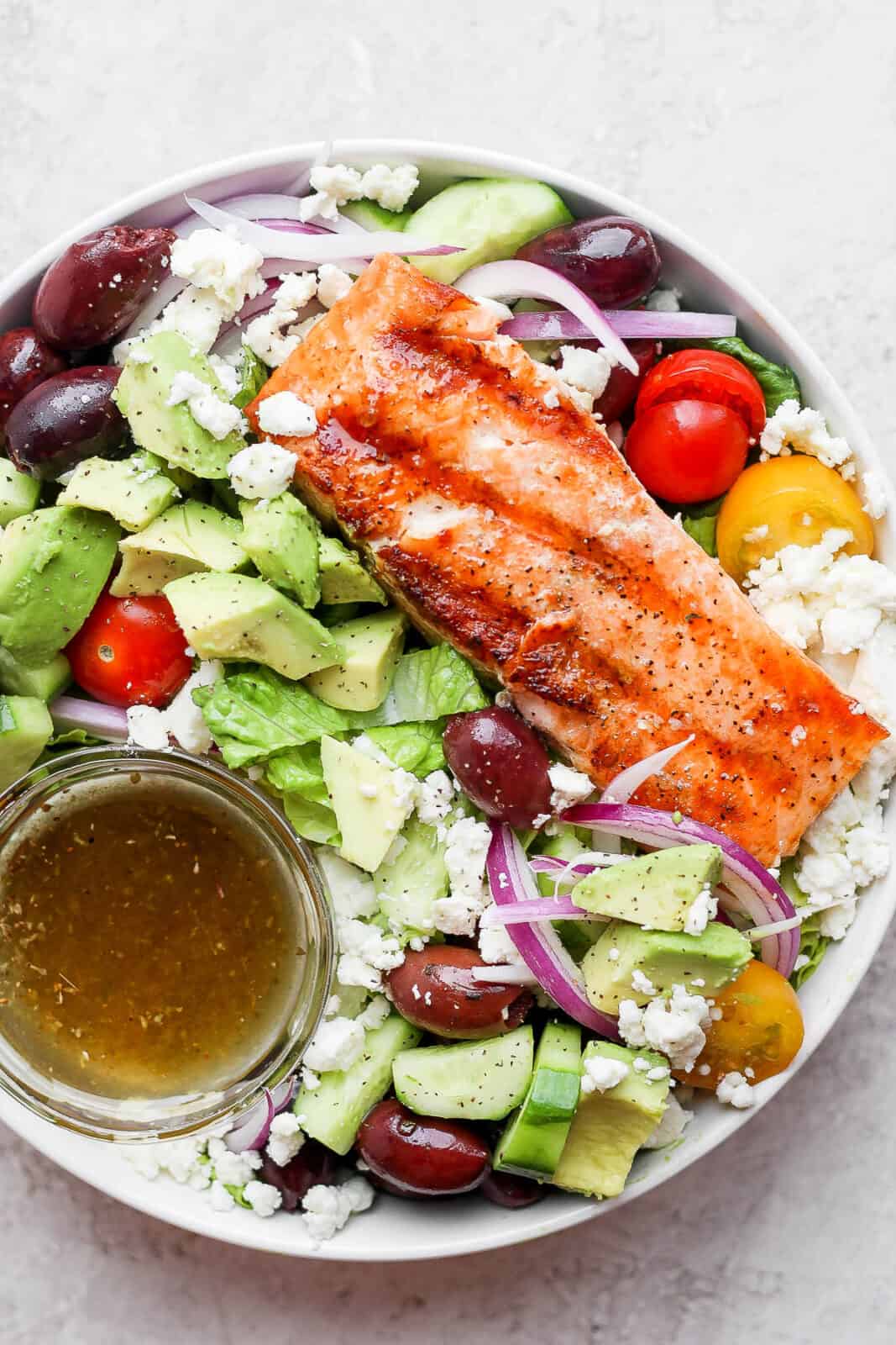 Bowl of grilled salmon salad with avocado, olives and feta cheese.