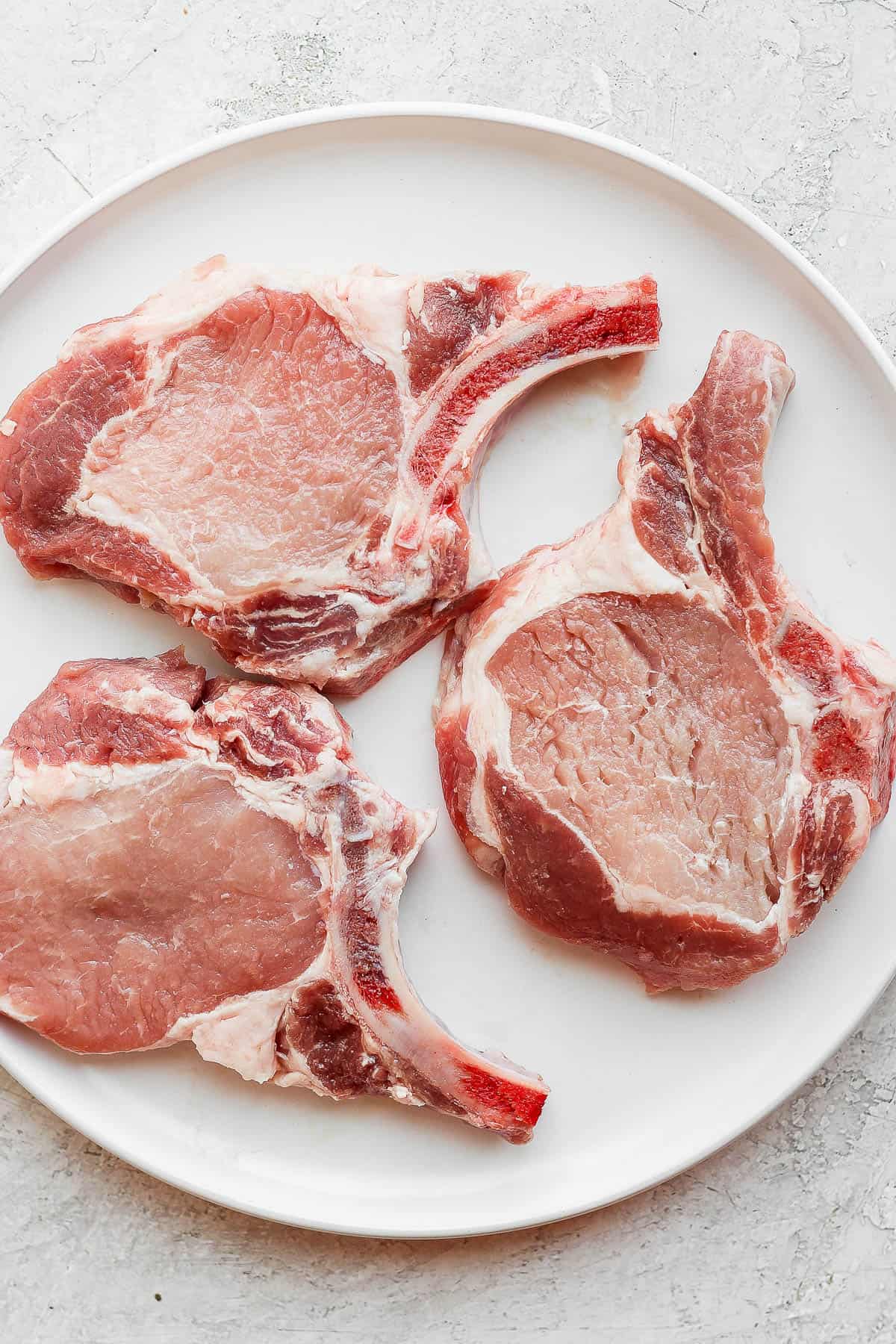 A plate of three raw pork chops. 