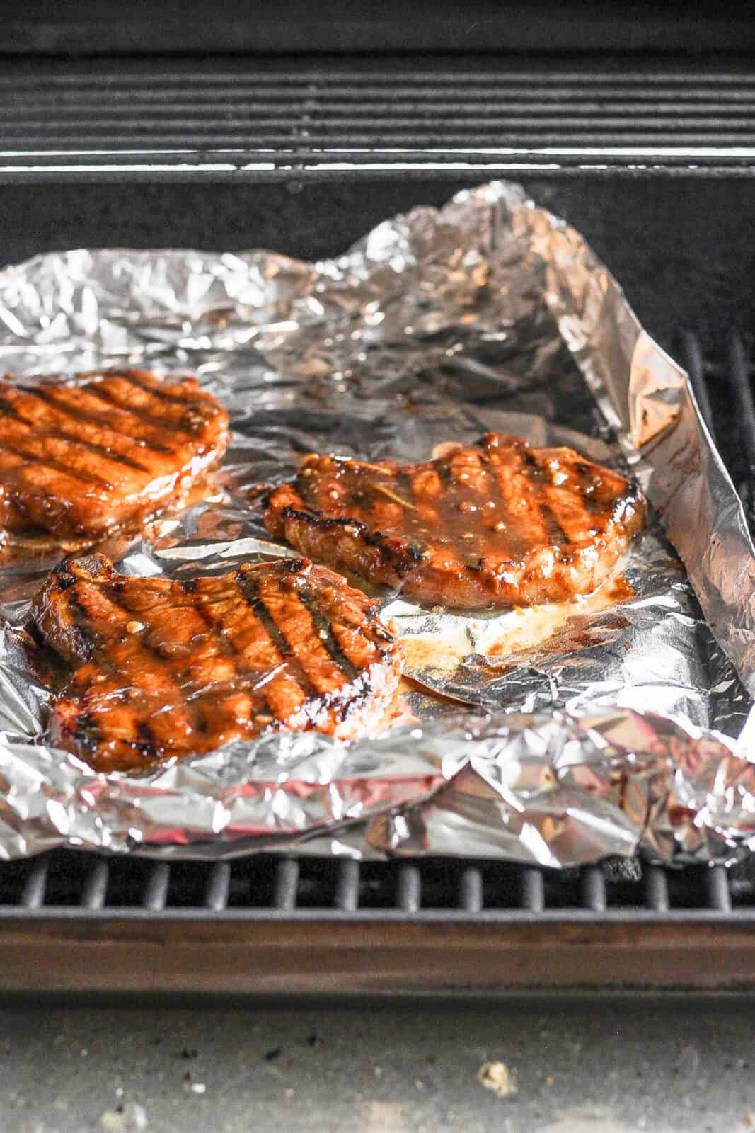 Pork chops cooking on the grill but in a foil tray. 