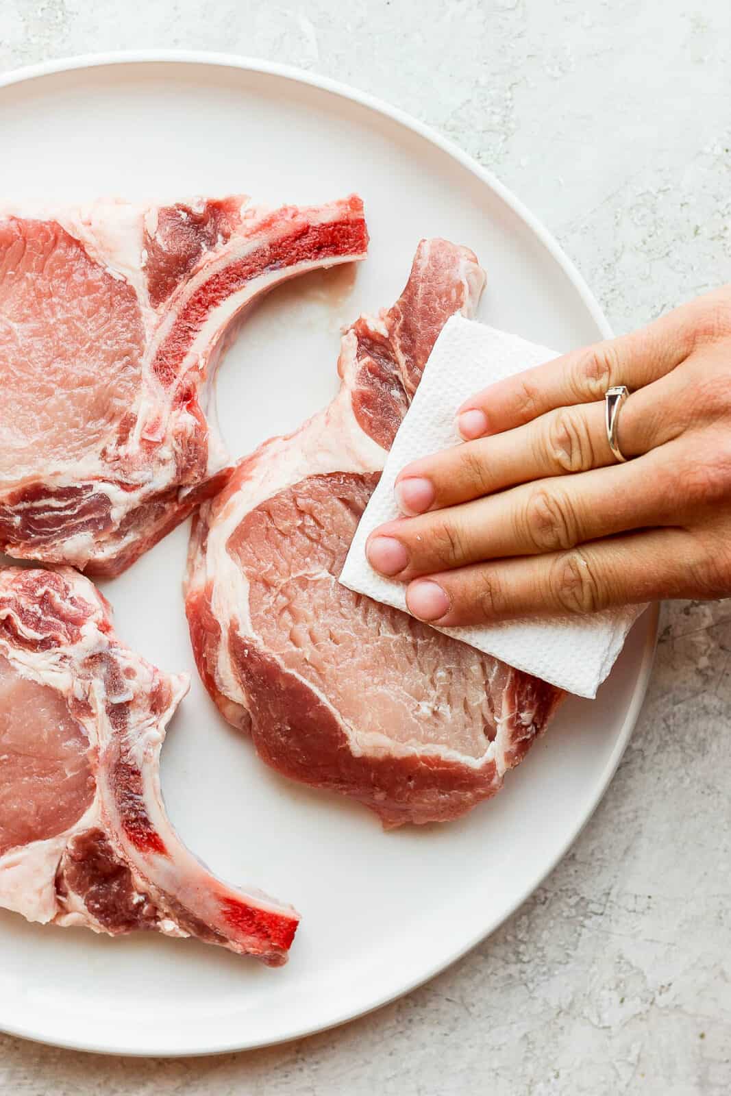 Pork chops being pat dry with a paper towel. 