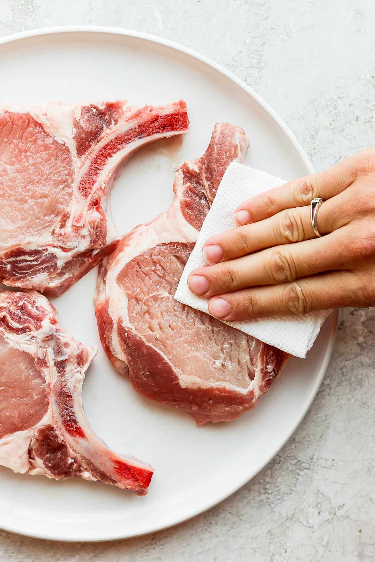 Someone patting a raw pork chop dry with a clean paper towel.