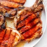 Four grilled pork chops on a plate with grill marks.