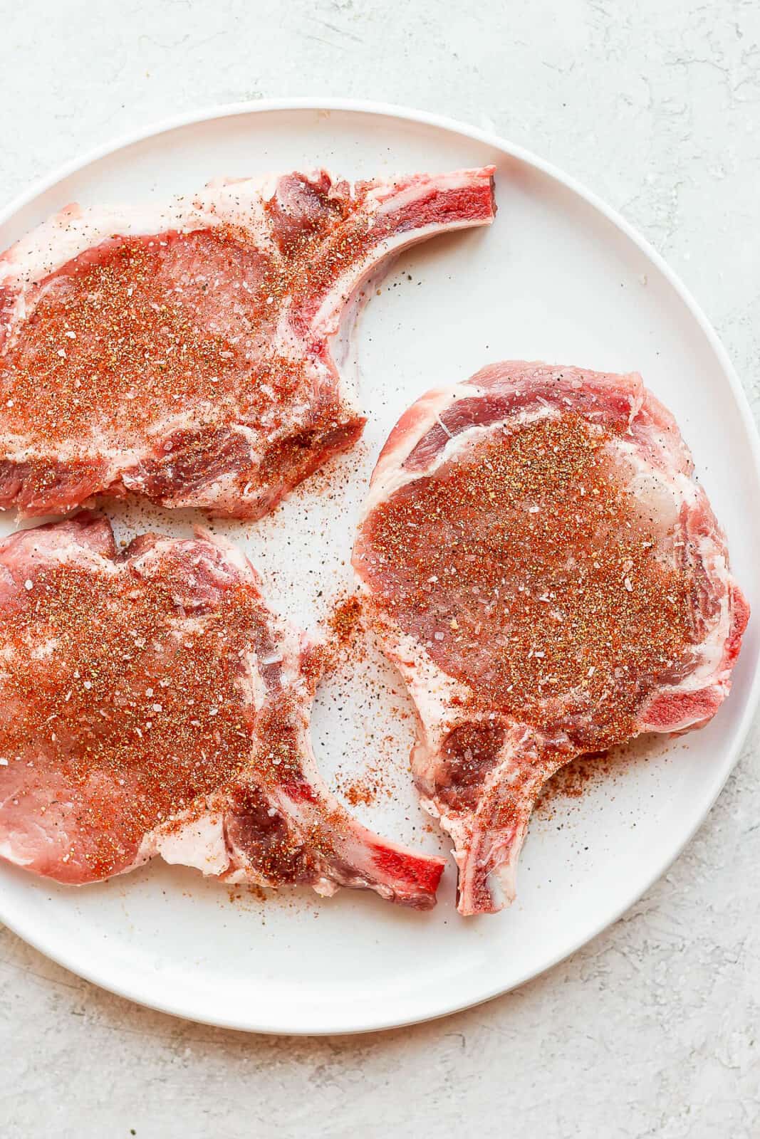 Raw pork chops with pork chop seasoning sprinkled on top.