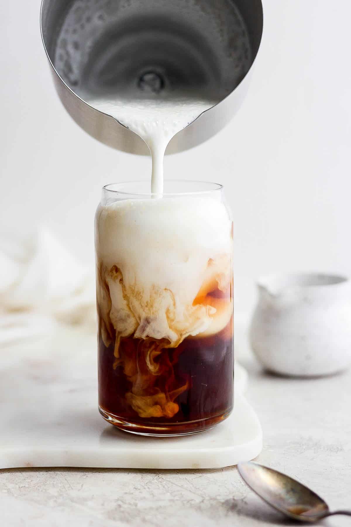Cold foam being poured into a glass of cold brew.