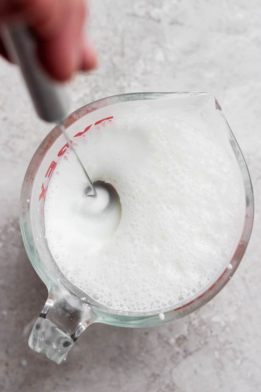 Handheld frother in a measuring cup with sweet cream cold foam ingredients.
