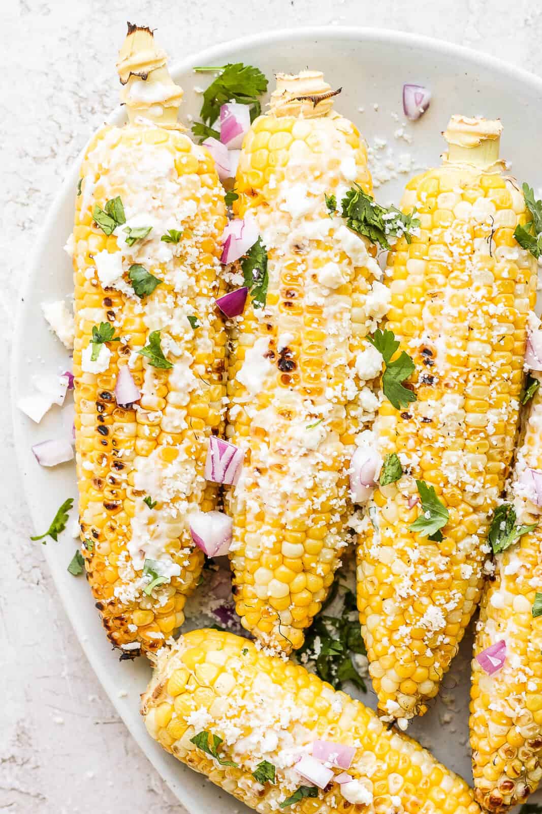 Grilled corn on the cob with mexican street corn topping on top.