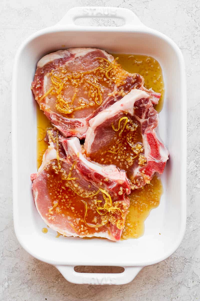 Raw pork chops in a dish with a pork chop marinade.