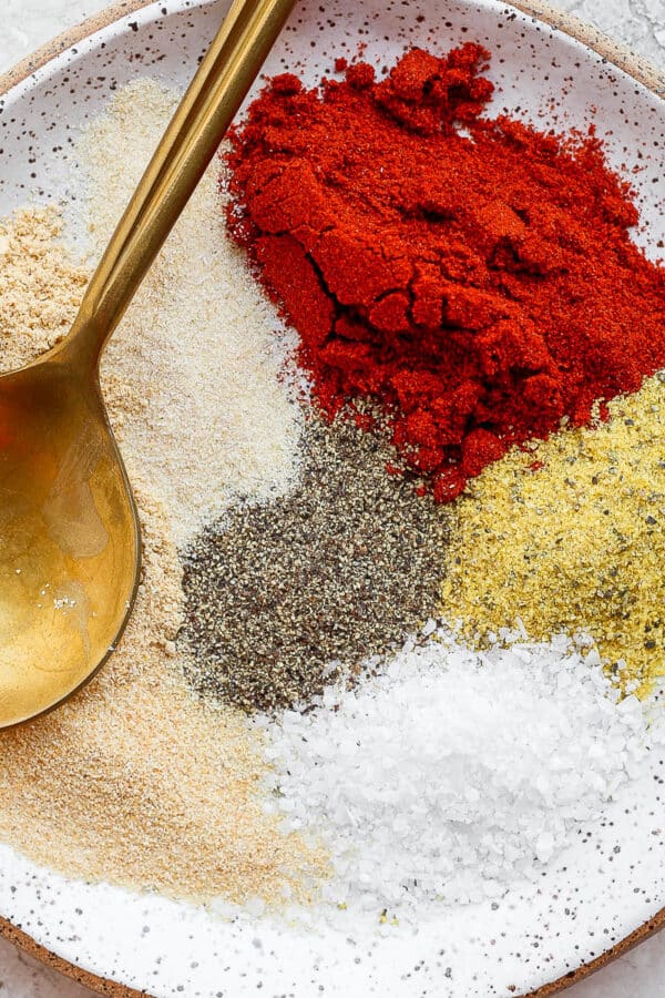 Spices for pork chop seasoning separated on a small plate with a gold spoon.