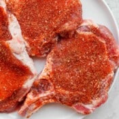Three pork chops covered in pork chop seasoning on a white plate.