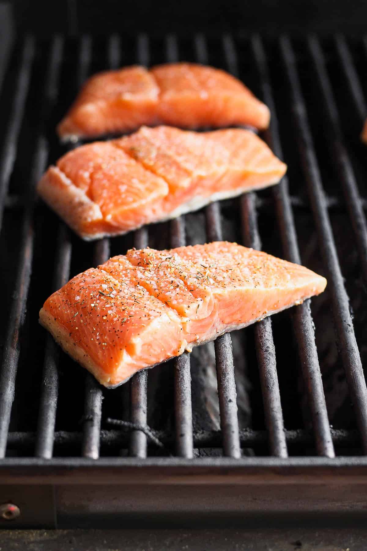 Salmon fillets on the grill with salmon seasoning on top.