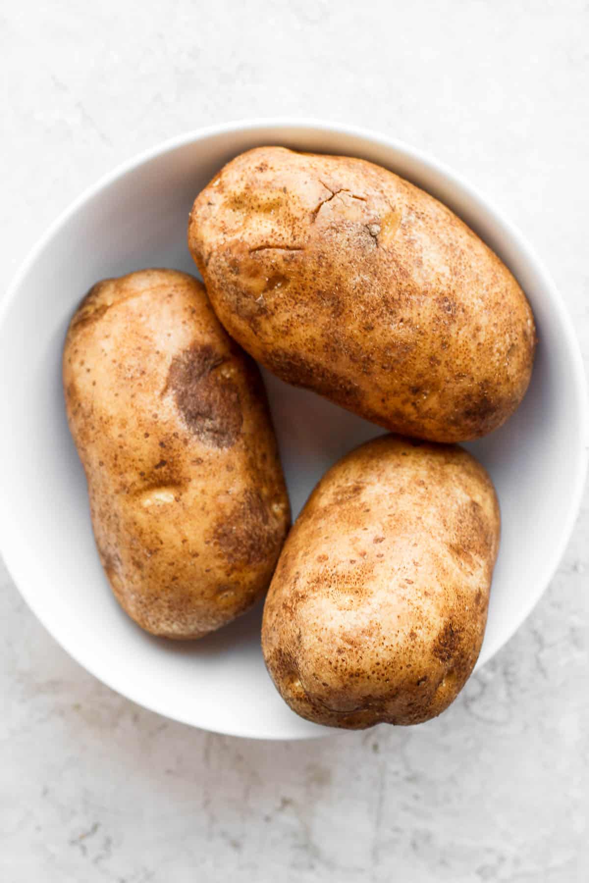 Three washed and dried potatoes in a white bowl.