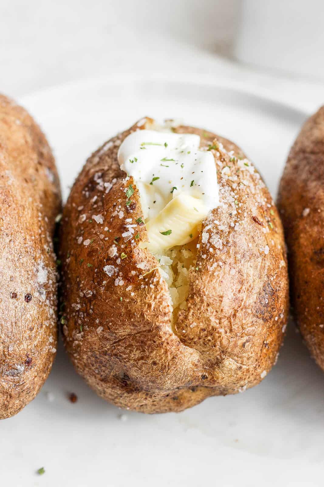 Close up of one oven baked potato cut down the middle filled with butter, sour cream, and light seasonings.