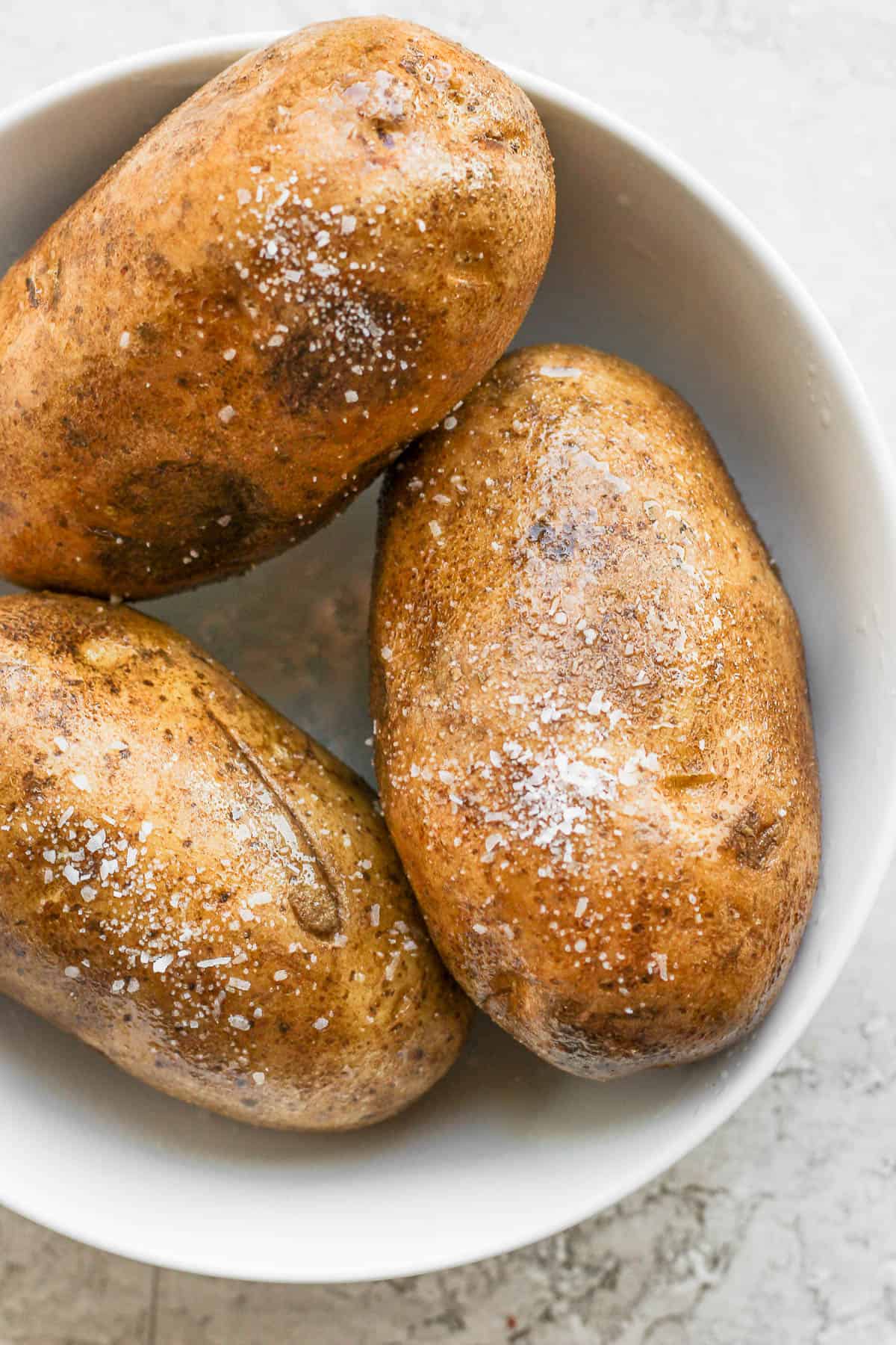 Whole baked potatoes in a white bowl.