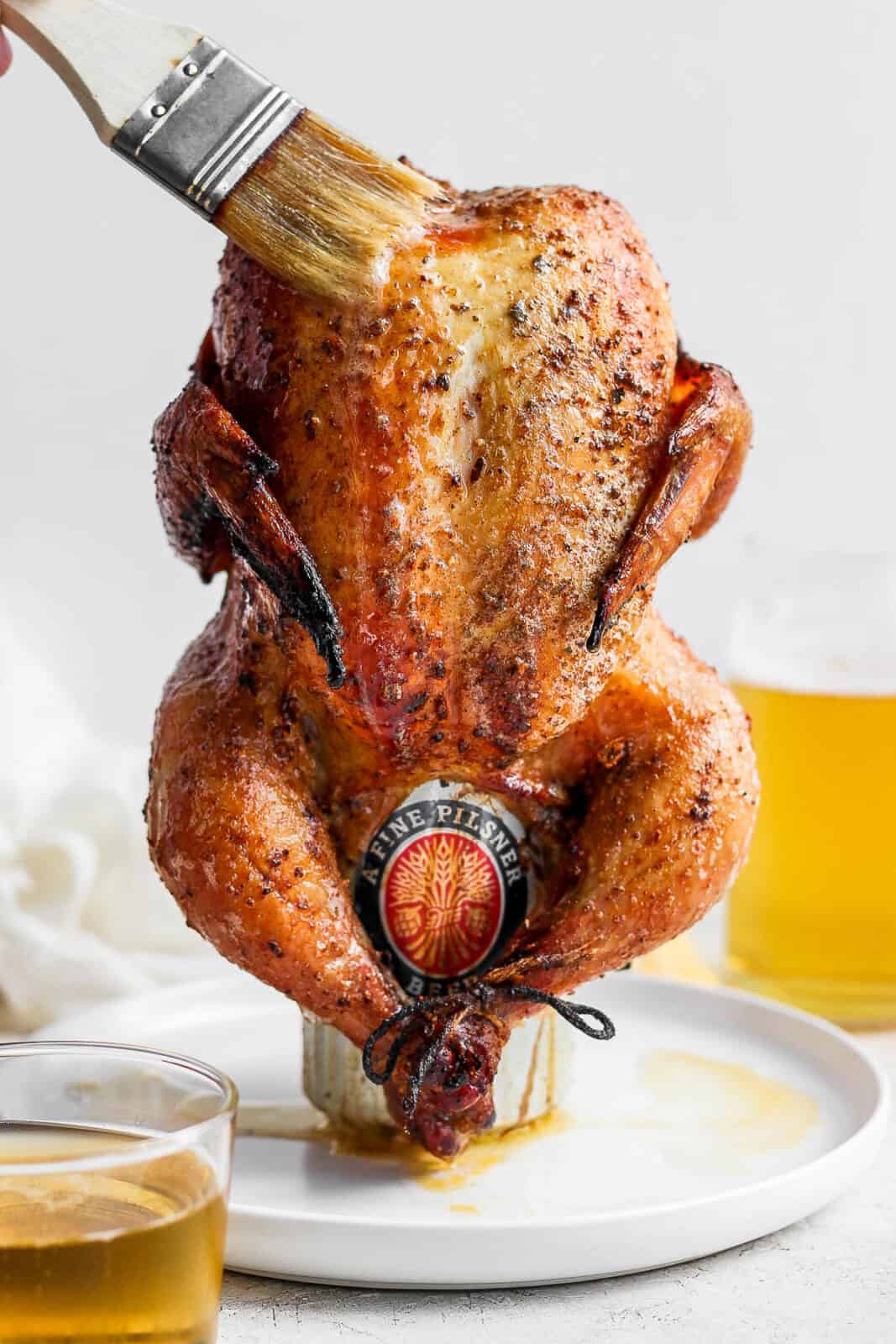 Smoked beer can chicken on a plate with someone brushing on melted butter.