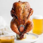 A beer can chicken on a plate with a glass of beer behind it.