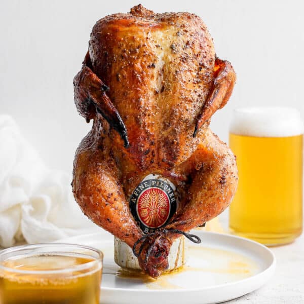 A beer can chicken on a plate with a glass of beer behind it.