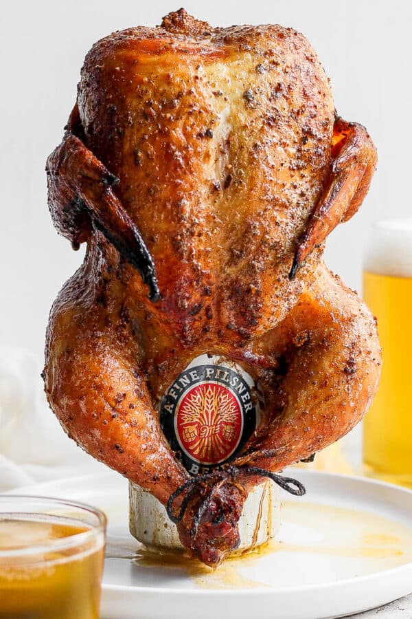 A beer can chicken on a plate with a glass of beer behind it.