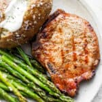 A plate with a smoked pork chop, baked potato and smoked asparagus.