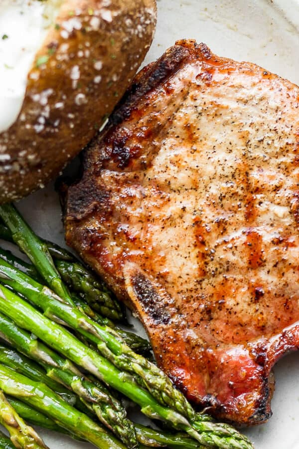 A plate with a smoked pork chop, baked potato and smoked asparagus.