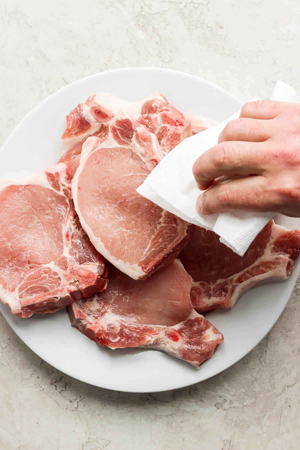 Someone patting raw pork chops dry with clean paper towel. 