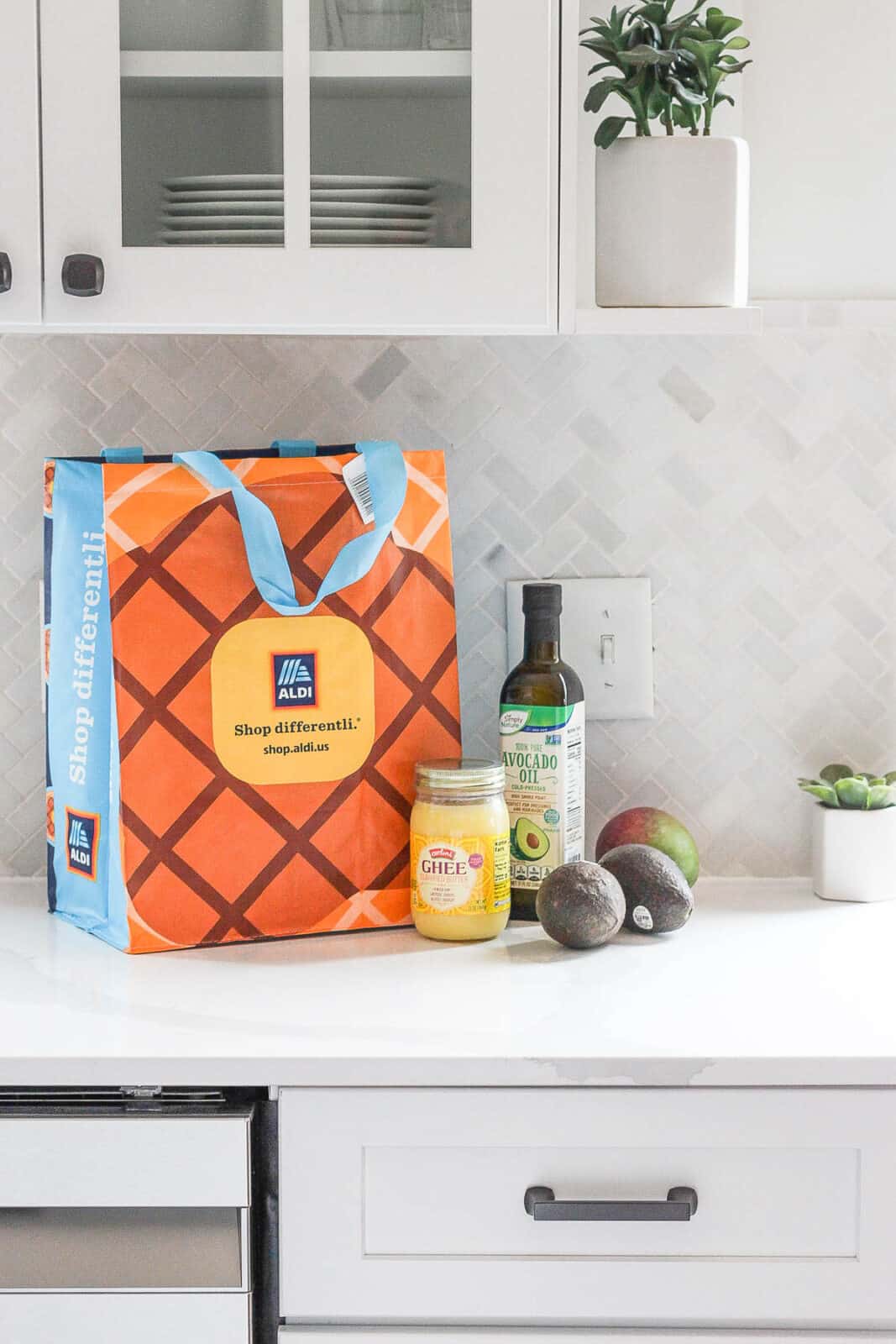 Aldi shopping bag, avocado oil, ghee, avocados, and a mango on the counter.