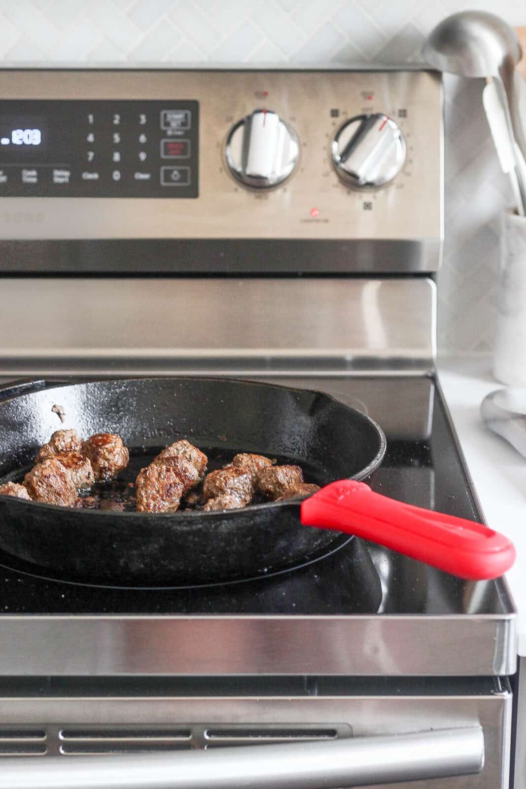 Meatballs cooking in a cast iron skillet on the stove top.