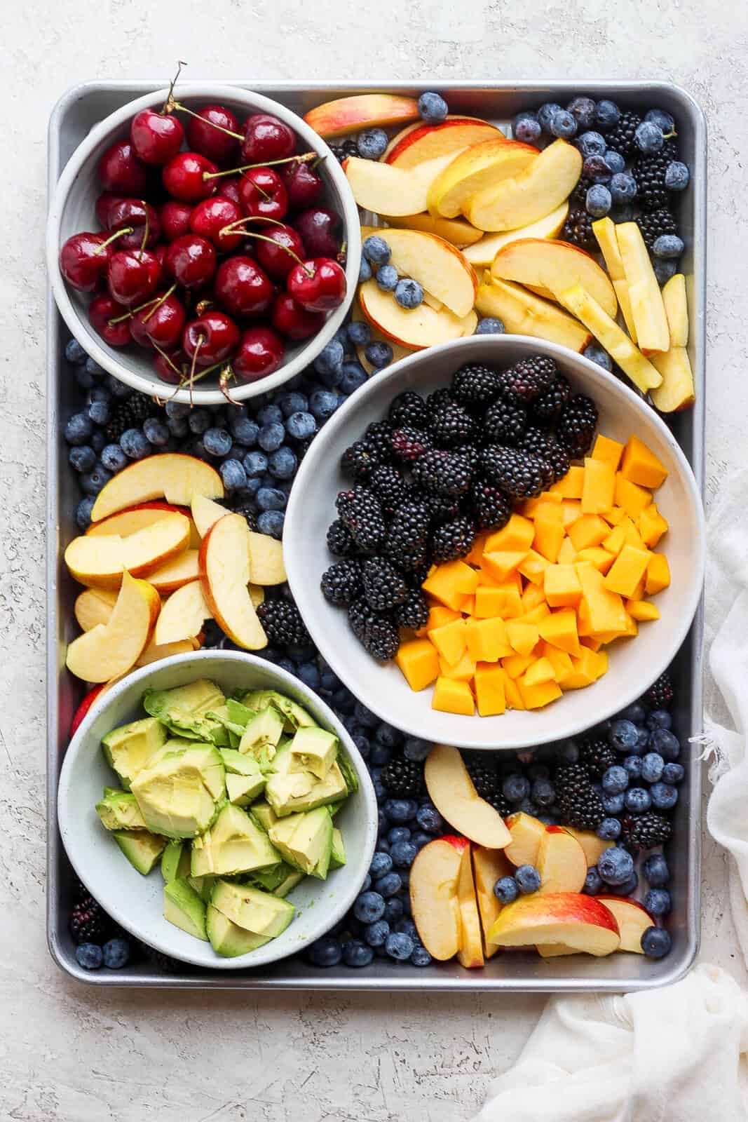 A baking sheet with cherries, blackberries, blueberries, cut up mango, apples, and avocado.